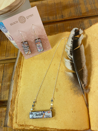 Berlin earrings & necklace laying atop of weathered leather journal with feather next to  necklace.